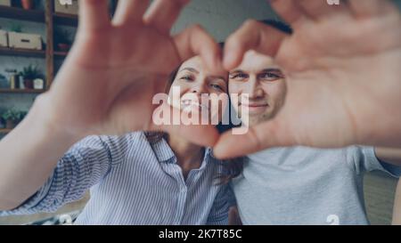 Porträt eines fröhlichen Paares, das mit den Händen Herz macht, die Kamera anschaut und lächelt. Romantische Beziehung, glückliches Eheleben und Flitterwochen-Konzept. Stockfoto