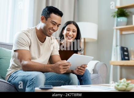 Wo auf der Erde habt ihr es gefunden. Ein junges Paar, das zu Hause auf dem Sofa sitzt und ein digitales Tablet benutzt. Stockfoto