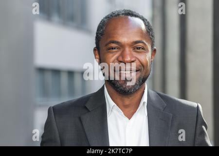 afroamerikanischer Geschäftsmann aus der Nähe, reifer Mann lächelnd und mit Blick auf die Kamera, Senior-Chef im Business-Anzug-Porträt, vor dem modernen Bürogebäude. Stockfoto
