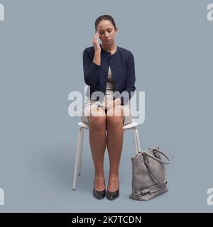 Junge Geschäftsfrau sitzt auf einem Stuhl und hat starke Kopfschmerzen Stockfoto