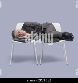 Erschöpfter Geschäftsmann legt sich auf Stühle und schläft Stockfoto