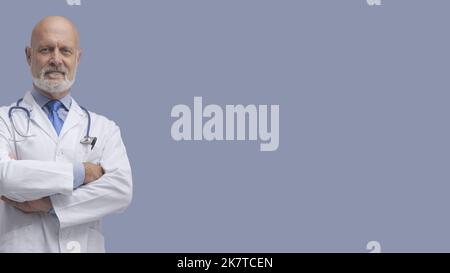 Oberarzt posiert mit gekreuzten Armen und lächelt, Medizin und Gesundheitskonzept Stockfoto