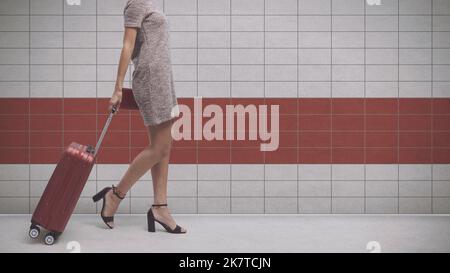 Junge, elegante Frau, die allein reist, zieht an der U-Bahn-Station ihre Trolley-Tasche, leerer Kopierraum Stockfoto