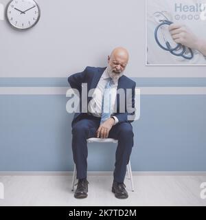 Patient, der im Wartezimmer des Krankenhauses sitzt: Der Mann hat starke Rückenschmerzen Stockfoto