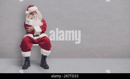 Gelangweilter Weihnachtsmann sitzt auf einem Stuhl und wartet auf ein Vorstellungsgespräch Stockfoto