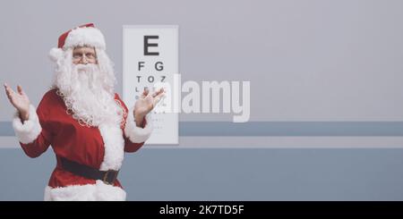 Fröhlicher Weihnachtsmann trägt eine Brille und einen Sehtest, ein Augenpflegekonzept, einen leeren Kopierraum Stockfoto