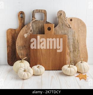 Küchenausstattung mit Schneidebrettern und Kürbissen. Alte Schneidebretter auf dem Tisch und weiße dekorative Kürbisse. Küche Herbst Stillleben. Stockfoto