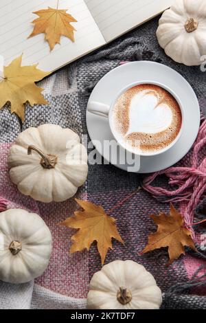 Weiße Kürbisse, Kaffee und Herbstblätter auf einem karierten Blatt. Einrichtung im Herbst. Stockfoto