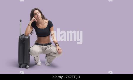 Junge Reisende Frau, die sich auf ihren Trolley-Koffer lehnt und wartet, ist müde und enttäuscht Stockfoto