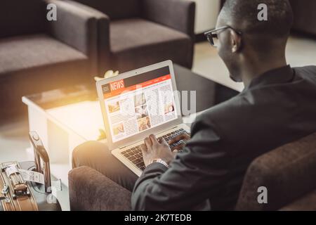 Ein Geschäftsmann las die News-Update-Website in einem Laptop, während er in der Flughafenlounge auf die Reise wartete Stockfoto