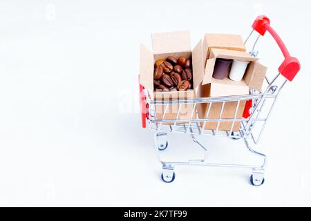 Kleine Pappkartons voller gerösteter Kaffeebohnen und Pappkaffeebechern in einem Miniatur-Schubkarren, isoliert auf weißem Hintergrund mit Platz für Kopien. Kaffee Stockfoto