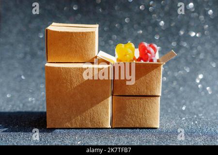 Zwei bunte Gummibären gucken aus einer Versandkiste isoliert auf einem schwarz glitzernden Hintergrund. Online-Kauf von Bonbons. Stockfoto