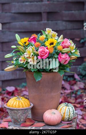 Bouquet mit rosa Rosen, Sonnenblumen, Lilienblumen und Saflor in Terrakotta-Topf im Herbstgarten Stockfoto