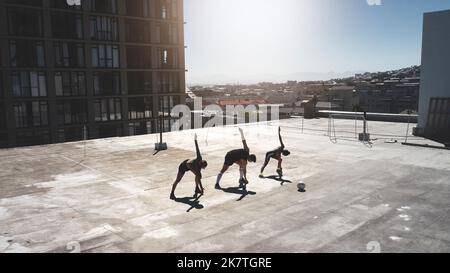 Fitness-Gruppe, Stretching und Ballsport mit Freunden, die an einem Sommertag auf dem Dach des Stadthauses trainieren, trainieren und sich aufwärmen. Athlet Mann und Stockfoto