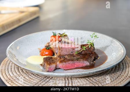 Medium Rare Beef Steak wurde gegrillt und mit Champignons und Minisomate auf einem weißen Gericht gebraten, fertig zum Servieren und Essen. Stockfoto