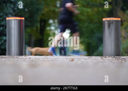 PRODUKTION - 17. Oktober 2022, Hamburg: Ein Jogger läuft mit einem Hund an einem Pollersystem im Stadtpark vorbei. Im Stadtpark wurde eine einfache Barriere durch das Pollersystem ersetzt. Seitdem ist es seit mehr als vier Jahren außer Betrieb und kostet rund 35.000 Euro für Reparatur und Wartung. Die Ausgabe 50. des Black Book of the Taxpayers' Association wird diesen Mittwoch veröffentlicht. Mit den aktuellen Fällen hat Hamburg seit 1973 182 Einträge. Foto: Marcus Brandt/dpa Stockfoto