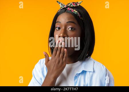 Betäubt afrikanisches Weibchen mit geöffnetem Mund erkennt schlechte Nachrichten vor gelbem Hintergrund Stockfoto
