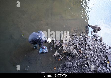 19. Oktober 2022, Hamburg: Ein Mitarbeiter des Landesamtes für Straßen, Brücken und Wasserstraßen legt Gegenstände, die in einer fast leeren Alsterflotte gefunden wurden, zur Entfernung an die Kaimauer. Die Alsterfleet wurde für die Inspektions- und Reinigungsarbeiten entwässert. Der Schiffsverkehr auf der Alsterfleet, der Bleichenfleet, der Mönkedammfleet, der Neuenwallfleet und der Herrengrabenfleet wurde eingestellt. Foto: Marcus Brandt/dpa Stockfoto