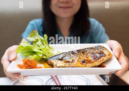 Asiatische Frau hält einen Teller mit gegrilltem saba-Fischsteak mit Teriyaki-Sauce im japanischen Restaurant Stockfoto