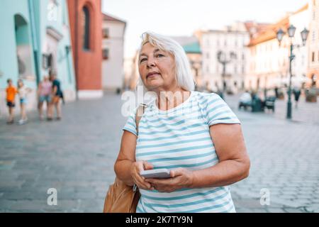 Frau aus dem mittleren Alter mit blonden Haaren und einem Lächeln auf dem Smartphone in der Altstadt von Krakau, Polen. Stockfoto