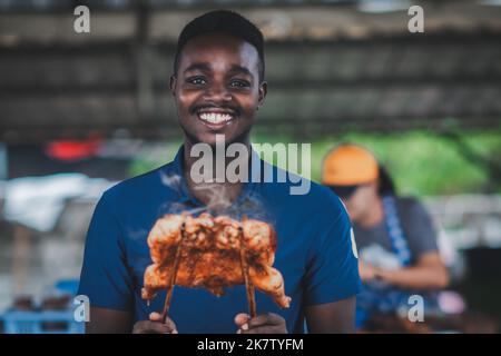 Afrikanischer Verkäufer, der gegrilltes Huhn verkauft, steht lächelnd Stockfoto