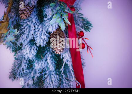 Weihnachtliche Dekoration mit Schnee, Evergreens, Kegelbällen und Feiertagsmotiven. Goldenes und rotes Band. Frohes neues Jahr und frohe Weihnachten. Stockfoto
