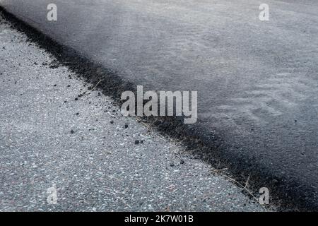 Frische schwarze und alte graue Asphaltschichten auf der Fahrbahn Textur diagonale Linie Nahaufnahme. Stockfoto