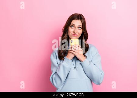 Portrait von ziemlich gesinnten Dame halten Telefon aussehen interessiert leeren Raum auf rosa Hintergrund isoliert Stockfoto