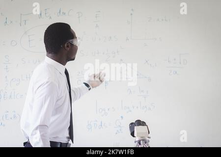Afrikanischer Lehrer erklärt den wissenschaftlichen Unterricht im Klassenzimmer mit Eine wissenschaftliche Gleichung im Hintergrund Stockfoto