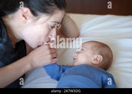 Nahaufnahme von Mutter, die die Hand ihres Babys küsst, während er sie anlächelt Stockfoto