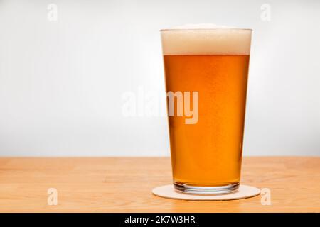 Volles Shaker Pint Glas Amber Ale oder Bier auf Holztisch mit grauem Hintergrund Stockfoto