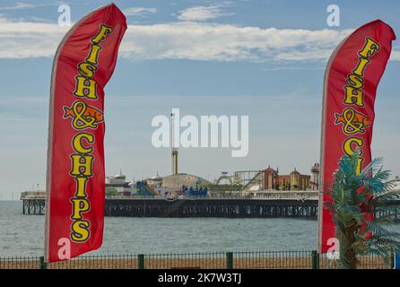 Flaggen für Fish and Chips am Strand von Brighton in East Sussex, England. Mit Pier im Hintergrund. Stockfoto