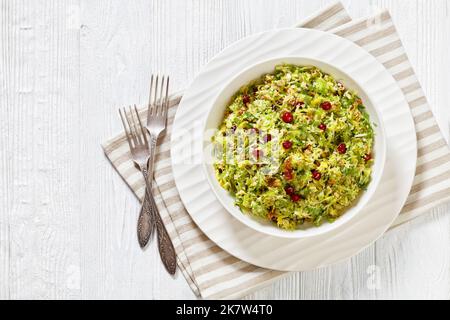 rosenkohl mit Mandeln, knusprig gebratenem Speck und Preiselbeeren in weißer Schale auf Holztisch mit Gabeln, horizontale Ansicht von oben, flach liegend Stockfoto