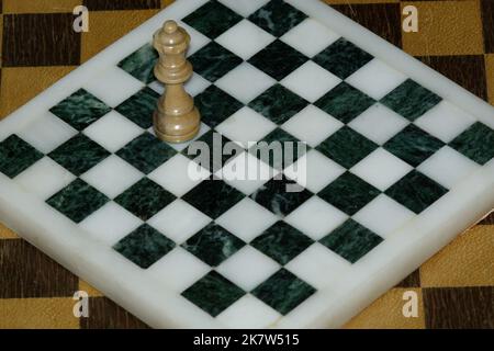 Einzelstück der Schachkönigin auf einem Quadrat in einem leeren Schachbrett, das ein Gefühl der Isolation hervorhebt. Die Königin ist zu groß für das Schachbrett - egoistisch. Stockfoto