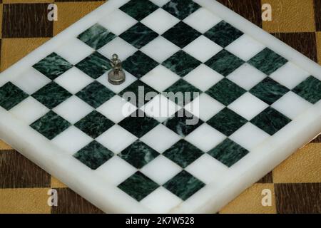 Lone Chess Pawn auf einem Quadrat in einem leeren Schachbrett, das ein Gefühl der Isolation hervorhebt. Schachbrett aus schwarzem und weißem Marmor mit Metallpfand. Stockfoto