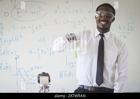 Afrikanischer Wissenschaftslehrer, der Experimente mit Flüssigkeiten im Kolben durchführt, Laborassistent in einer Brille, die chemische Reaktionen im Unterricht zeigt, Chemie Stockfoto