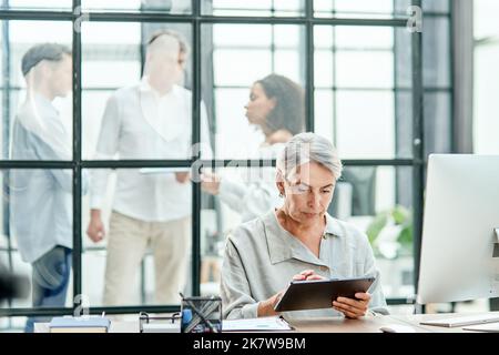 Eine Geschäftsfrau mit einem Klemmbrett sitzt an einem Schreibtisch. Stockfoto