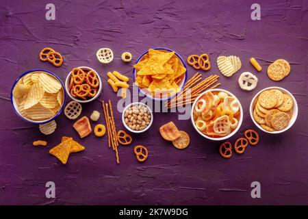 Salzige Snacks. Party Food Mix Hintergrund. Kartoffel- und Tortilla-Chips, Cracker und andere Vorspeisen in Schüsseln, darüber liegende flache Schuss Stockfoto