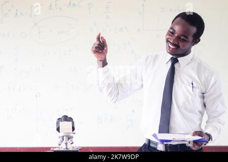 Die afrikanische Lehrerin Smile erklärt den Unterricht in der Wissenschaft im Klassenzimmer mit einer wissenschaftlichen Gleichung im Hintergrund Stockfoto