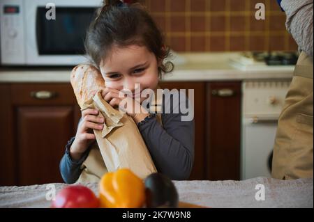 Nahaufnahme eines niedlichen kleinen Mädchens, das einen Laib Sauerteig aus der Bäckerei der Familie umarmt, während es den Lebensmittelbeutel auspackelt Stockfoto