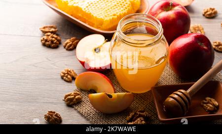 Einmachglas mit Honig, Honigtaube, Honigwabe, roten Äpfeln und Walnüssen auf Küchentisch Stockfoto