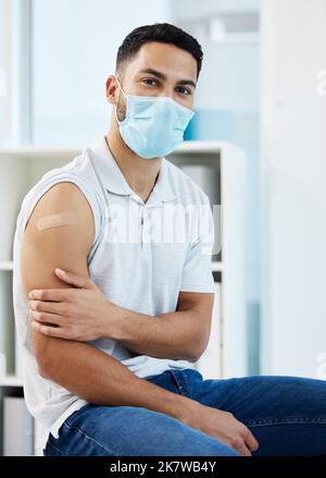 Ich fühlte kaum etwas. Ein junger Mann, der eine Gesichtsmaske trägt und allein sitzt, nachdem er in der Klinik seinen Covid-Impfstoff erhalten hat. Stockfoto