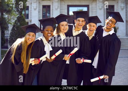 Lachend aufgeregt Gruppe von multikulturellen Menschen in Abschlusskleider und Mützen im Freien auf dem Campus. Stockfoto