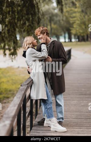 In voller Länge Rotschopf Mann und blonde Frau im Mantel umarmt, während mit Datum im Park, Stock Bild Stockfoto