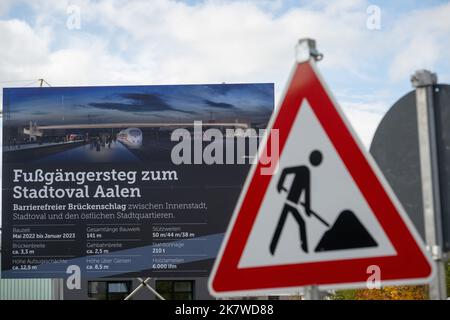 19. Oktober 2022, Baden-Württemberg, Aalen: Vor der Bautafel eines Fußgängerwegs über die Gleise des Bahnhofs Aalen steht ein Baustellenschild. In seinem schwarzen Buch über diese Konstruktion kritisiert der Steuerzahler-Verband die Kostenerhöhung von drei auf zehn Millionen Euro. Foto: Stefan Puchner/dpa Stockfoto