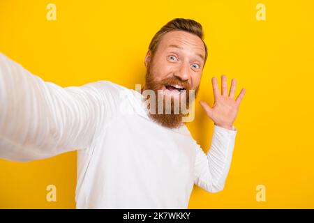 Foto-Porträt von schönen jungen Mann machen Selfie-Front-Kamera Welle Hand hallo tragen stilvolle weißen Pullover isoliert auf gelbem Hintergrund Stockfoto