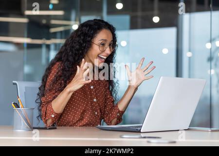 Junge hispanische Geschäftsfrau hat gute Arbeitsergebnisse, Geschäftsfrau ist glücklich und feiert den Sieg, indem sie die Hände hoch hält und vom Laptop-Bildschirm liest. Stockfoto