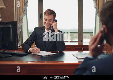Rezeptionist und Kunde an der Rezeption telefonieren in einem Luxushotel Stockfoto