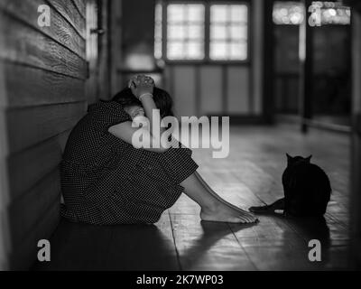 Traurige einsame kleine Mädchen weinen, während auf dem Boden sitzen in dunklen Raum mit einer Haltung der Traurigkeit und schwarze Katze sitzen mit ihr.Konzept der Depression oder Stockfoto