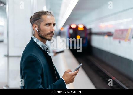 Geschäftsmann mit einem Smartphone, das auf der U-Bahn-Plattform steht. Stockfoto